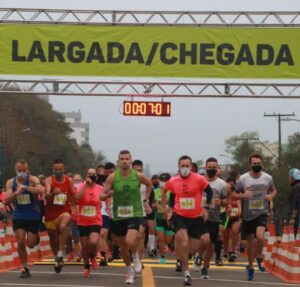 Largada de corrida de rua com estrutura de pórtico, banners e materiais promocionais no percurso
